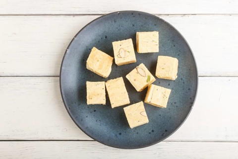 Traditional indian candy soan papdi in a blue ceramic plate with almond and pistache on a white