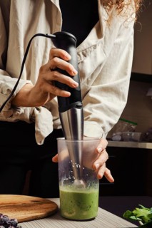 Unrecognizable woman using blender in the kitchen to make banana and spinach smoothie