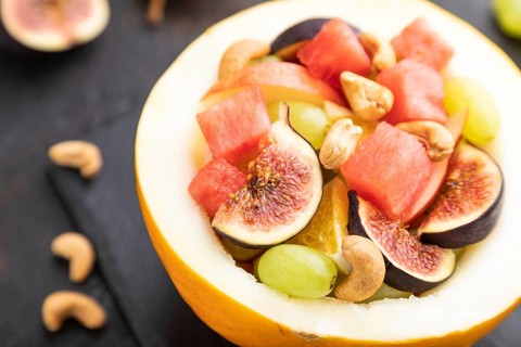 Vegetarian fruit salad of watermelon, grapes, figs, pear, orange, cashew on slate board on a black