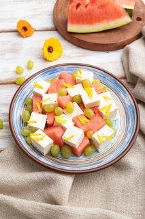 Vegetarian salad with watermelon, feta cheese, and grapes on blue ceramic plate on white wooden