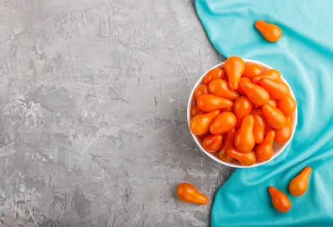 Fresh orange grape tomatoes in white ceramic bowl on gray concrete background with blue textile.