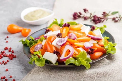 Vegetarian salad with fresh grape tomatoes, feta cheese, lettuce and onion on blue ceramic plate on