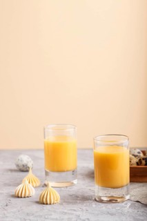 Sweet egg liqueur in glass with quail eggs and meringues on a gray and orange background. Side