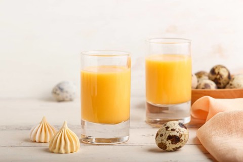 Sweet egg liqueur in glass with quail eggs and meringues on white wooden background. Side view,