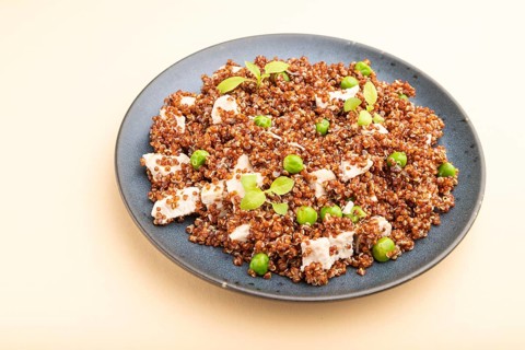 Quinoa porridge with green pea and chicken on ceramic plate on a pastel orange background. Side