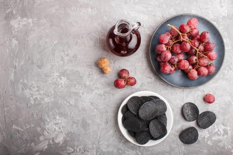 Black potato chips with charcoal, balsamic vinegar in glass, red grapes on a blue ceramic plate on