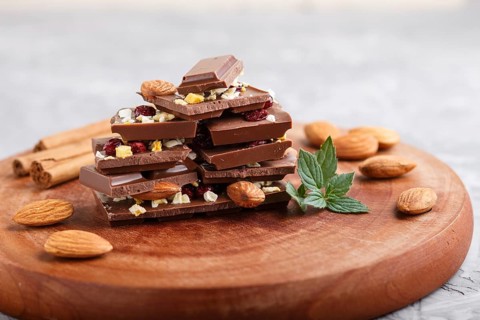 A pieces of milk chocolate with almonds and dried fruits on a brown wooden board on a gray concrete