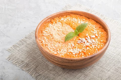 Carrot cream soup with sesame seeds in wooden bowl on a gray concrete background with linen textile