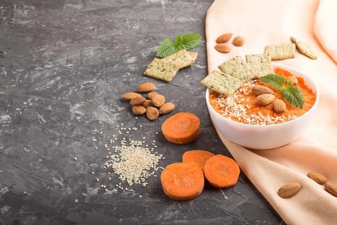 Carrot cream soup with sesame seeds, almonds and snacks in white bowl on a black concrete