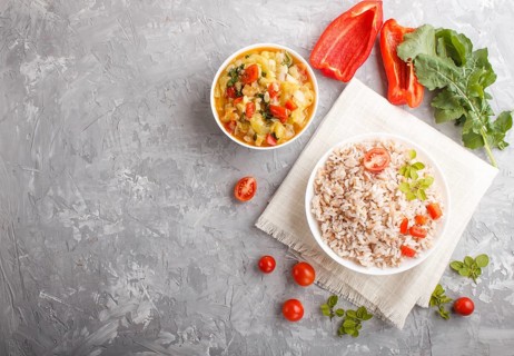 Unpolished rice porridge with stewed vegetables and oregano in white bowl on a gray concrete