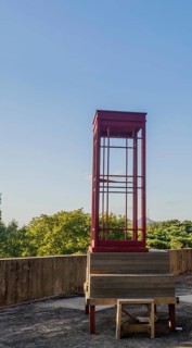 Red wooden telephone booth minus phone and without glass on roof of building on sunny day with blue