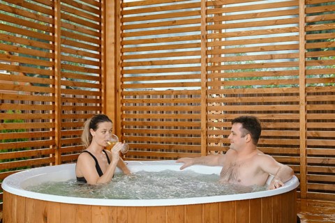 Beautiful couple in love relaxing and drinking wine in outdoor hot tub during weekend