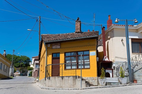 Small house with orange-painted facade and wooden windows on a quiet street, Soufli, Eastern
