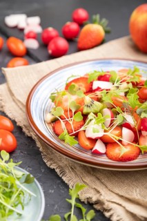 Vegetarian fruits and vegetables salad of strawberry, kiwi, tomatoes, microgreen sprouts on black