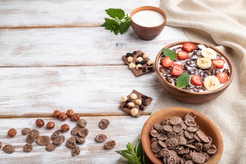 Chocolate cornflakes with milk and strawberry in wooden bowl on white wooden background and linen