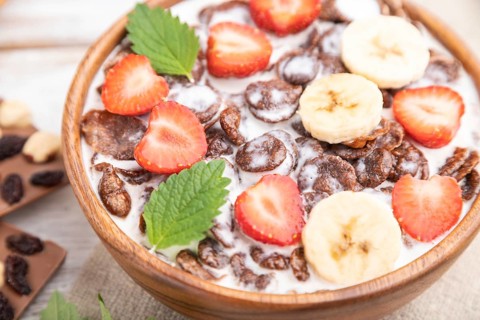 Chocolate cornflakes with milk and strawberry in wooden bowl on white wooden background and linen