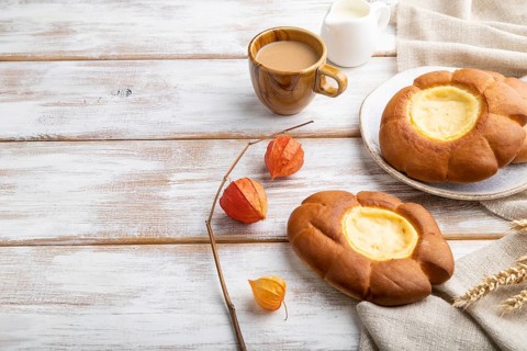 Sour cream bun with cup of coffee on a white wooden background and linen textile. Side view, copy