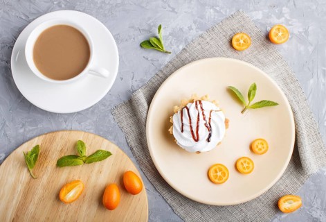 Cake with whipped egg cream on a light brown plate with kumquat slices and mint leaves on a gray