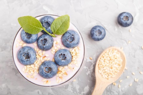 Yoghurt with blueberry and sesame in a glass and wooden spoon on gray concrete background. top