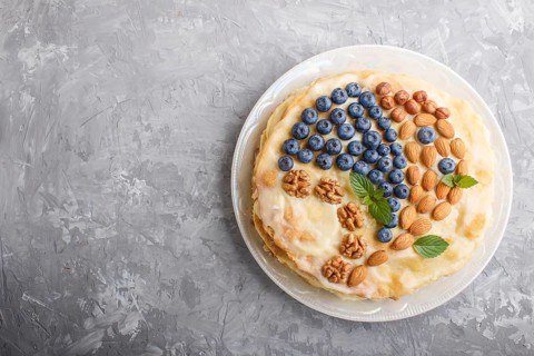 Homemade layered Napoleon cake with milk cream. Decorated with blueberry, almonds, walnuts,