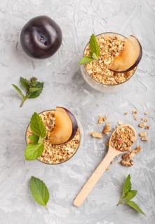Yoghurt with plum, chia seeds and granola in a glass and wooden spoon on gray concrete background.
