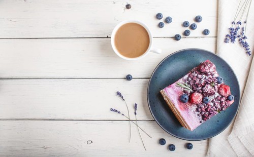 Berry cake with milk cream and blueberry jam on blue ceramic plate with cup of coffee and fresh