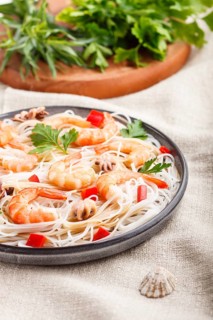 Rice noodles with shrimps or prawns and small octopuses on gray ceramic plate on a white linen