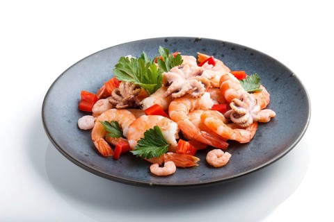 Boiled shrimps or prawns and small octopuses with herbs on a blue ceramic plate isolated on white