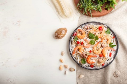 Rice noodles with shrimps or prawns and small octopuses on gray ceramic plate on a white wooden