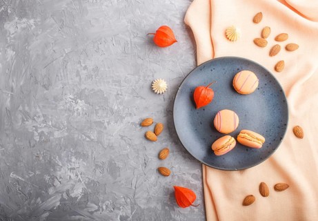 Orange macarons or macaroons cakes on blue ceramic plate on a gray concrete background and orange