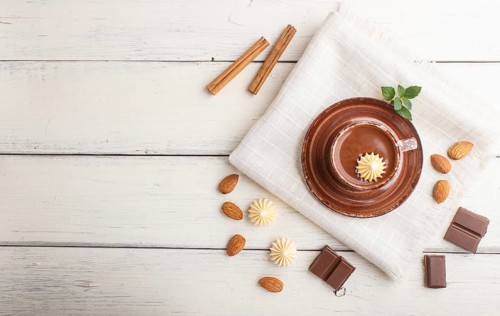 Cup of hot chocolate and pieces of milk chocolate with almonds on a white wooden background with