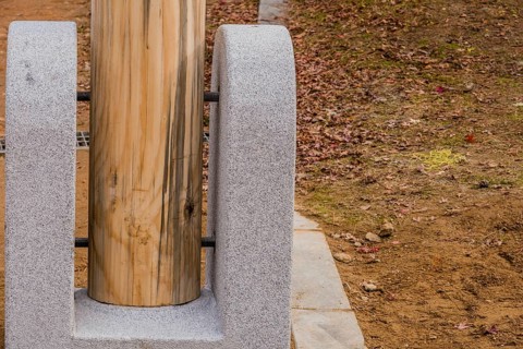 Closeup of bottom of unpainted wooden post held in concrete footing with large threaded bolts in
