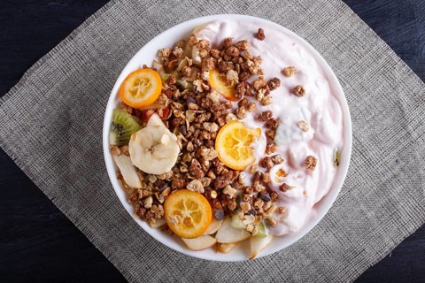 Vegetarian salad of bananas, apples, pears, kumquats, kiwi with granola and yogurt on black woodem