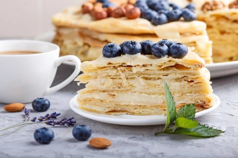 Homemade layered Napoleon cake with milk cream. Decorated with blueberry, almonds, walnuts,
