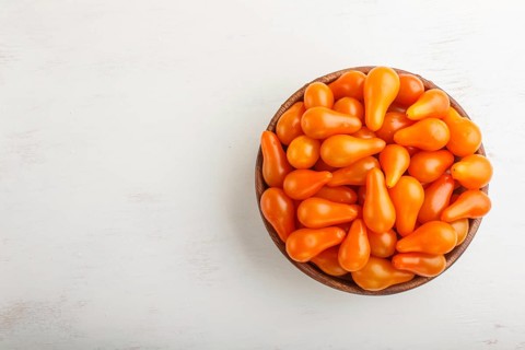 Fresh orange grape tomatoes in wooden bowl on white wooden background. top view, flat lay, copy
