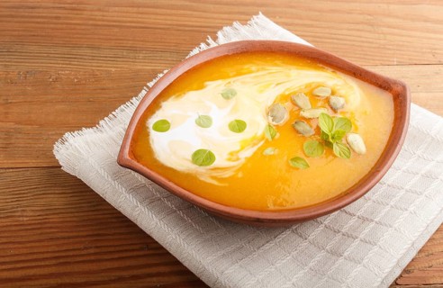 Traditional pumpkin cream soup with seeds in clay bowl on a brown wooden background with linen