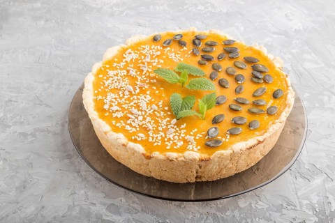 Traditional american sweet pumpkin pie decorated with mint, sesame and pumpkin seeds on a gray