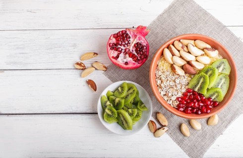 A plate with muesli, kiwi, pomegranate, Brazil nuts on a white wooden background. top view. copy