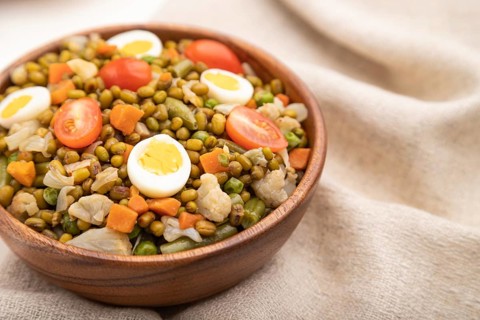 Mung bean porridge with quail eggs, tomatoes and microgreen sprouts on a white wooden background
