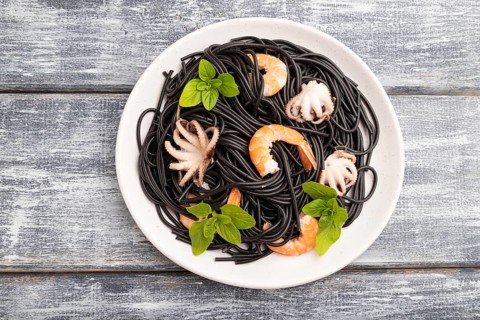 Black cuttlefish ink pasta with shrimps or prawns and small octopuses on gray wooden background.