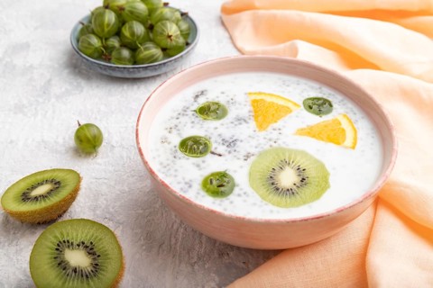 Yogurt with kiwi, gooseberry, chia in ceramic bowl on gray concrete background and orange linen
