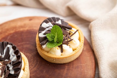 Sweet tartlets with chocolate and cheese cream with cup of coffee on a white wooden background and