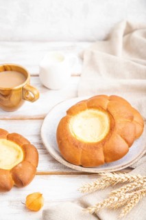 Sour cream bun with cup of coffee on a white wooden background and linen textile. Side view, close