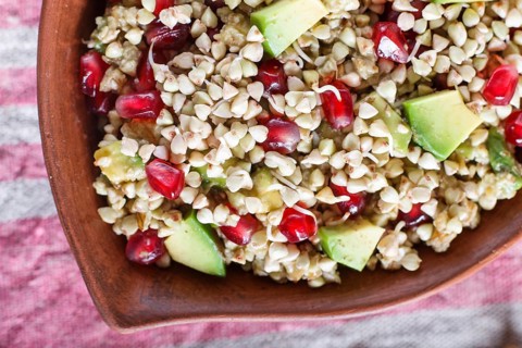 Salad of germinated buckwheat, avocado, walnut and pomegranate seeds in clay plate on white wooden