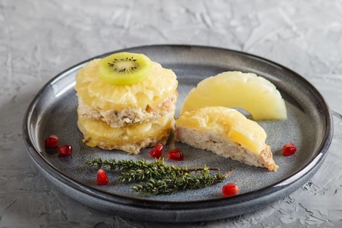 Pieces of baked pork with pineapple, cheese and kiwi on gray plate, side view, close up, selective