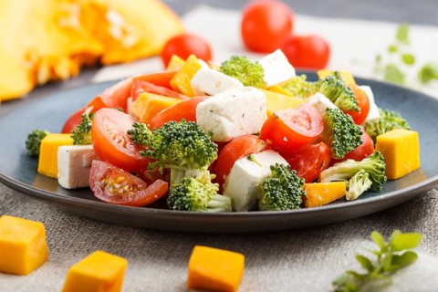 Vegetarian salad with broccoli, tomatoes, feta cheese, and pumpkin on a blue ceramic plate on a