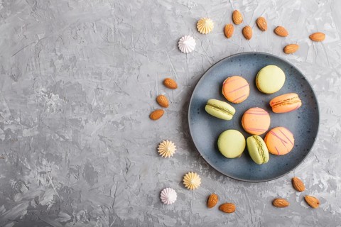 Orange and green macarons or macaroons cakes on blue ceramic plate on a gray concrete background.