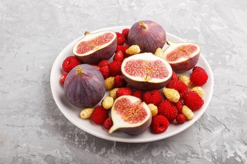 Fresh figs, strawberries and raspberries on white ceramic plate on gray concrete background. side