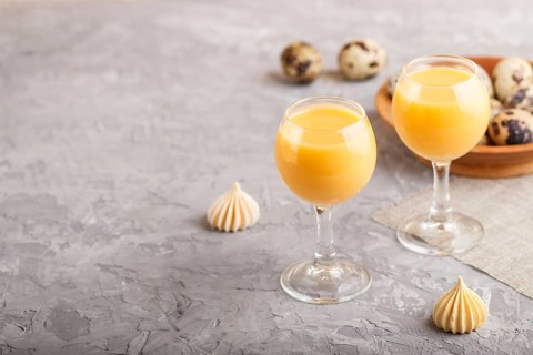 Sweet egg liqueur in glass with quail eggs and meringues on a gray concrete background. Side view,