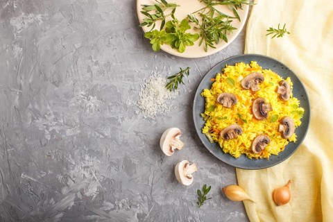 Yellow fried rice with champignons mushrooms, turmeric and oregano on blue ceramic plate on a gray